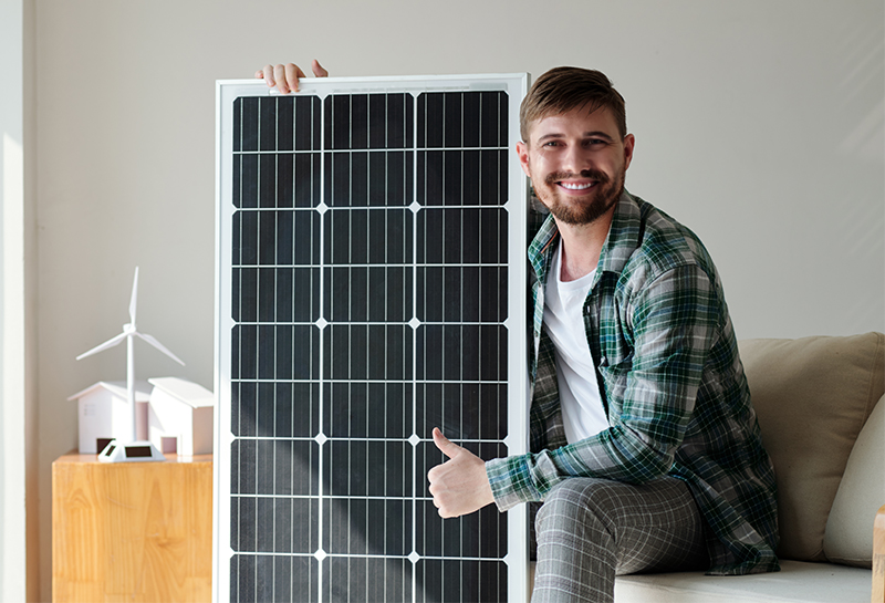 Ein junger Mann hebt grinsend ein Solarmodul und zeigt den Daumen nach oben.